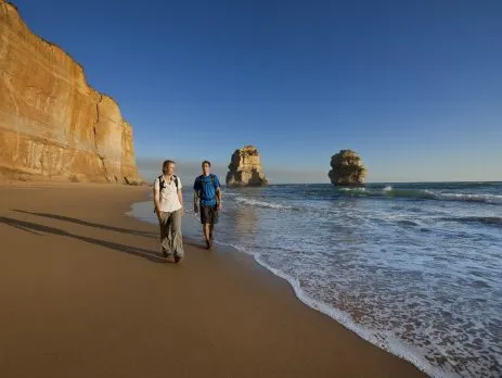 Travellers walking beside limestone stacks on the Great Ocean Road